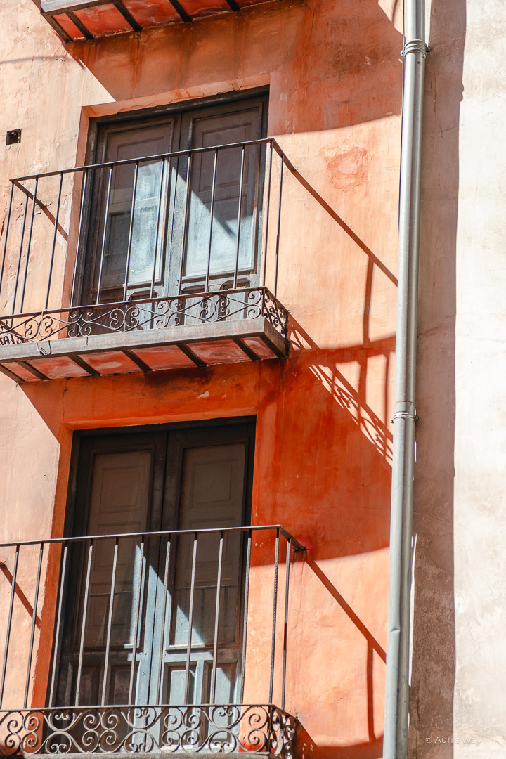 Balcon des rascacielos de Cuenca à la façade rouge, projetant les ombres laissées par la balustrade en fer.