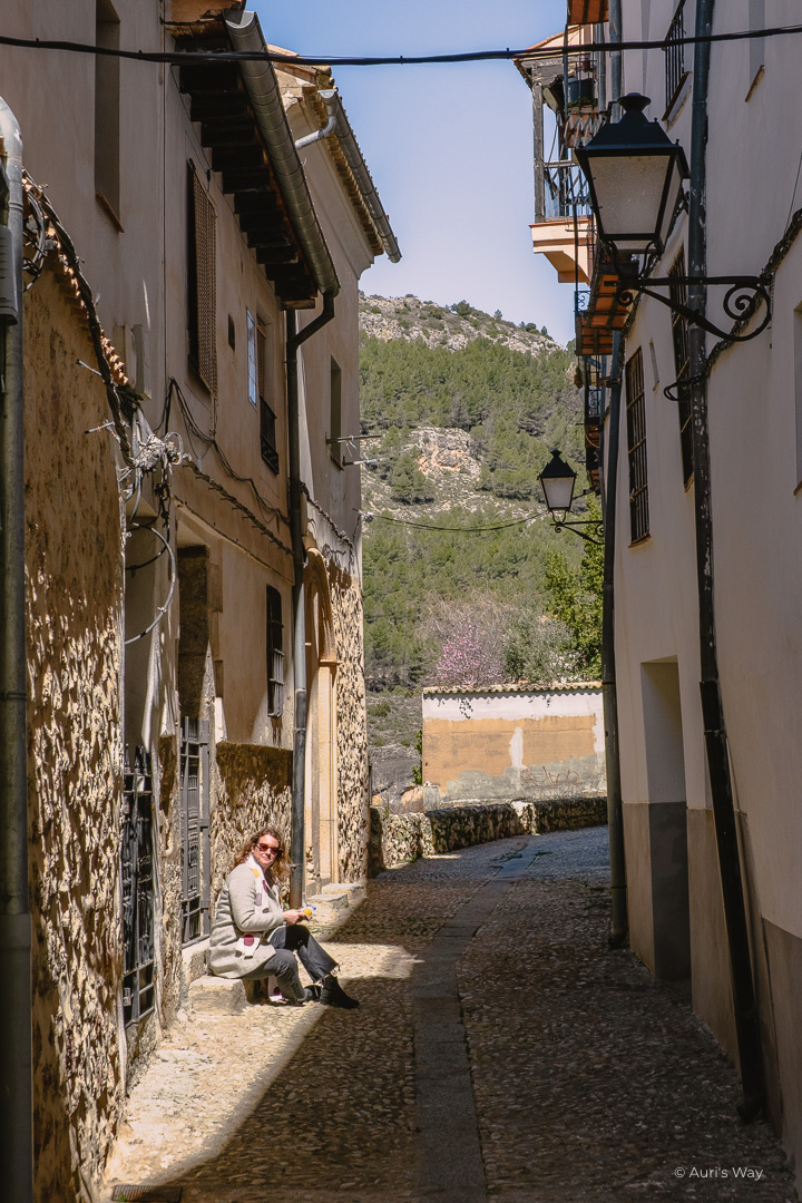 Jeune femme assise sur les marches d'une petite rue pavée du barrio de San Miguel à Cuenca, dans un rayon de soleil.