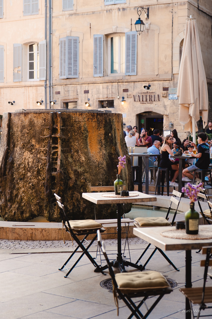 Fontaine moussue entourée par les tables de restaurants en haut de la place des Cardeurs à Aix-en-Provence.